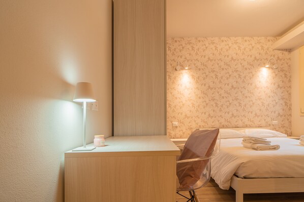 Habitación de hotel con escritorio de madera, una silla, una cama con toallas ordenadas y dos luces fijadas a la pared.
