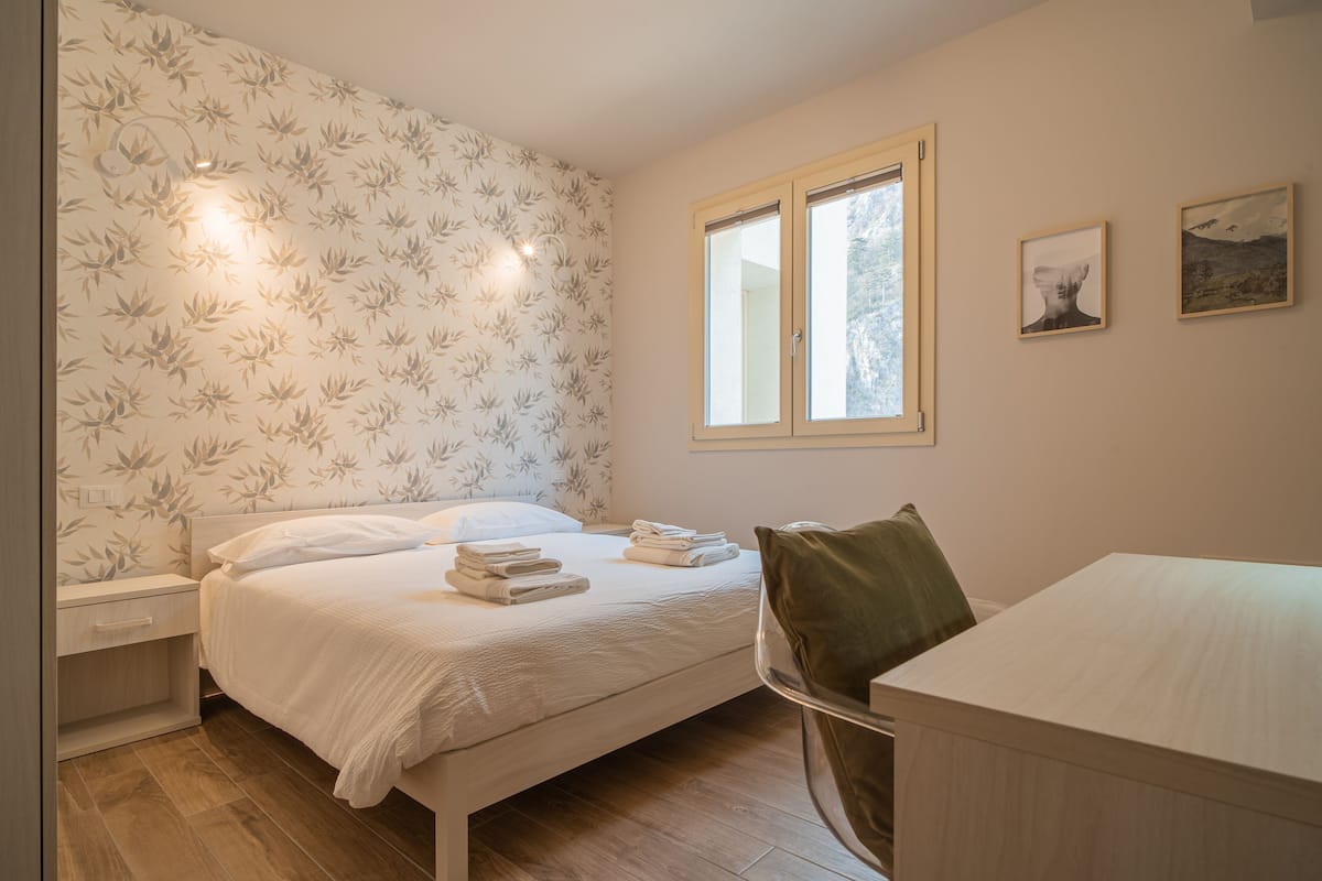 A bedroom with a bed, bedside table, chair, and a window.