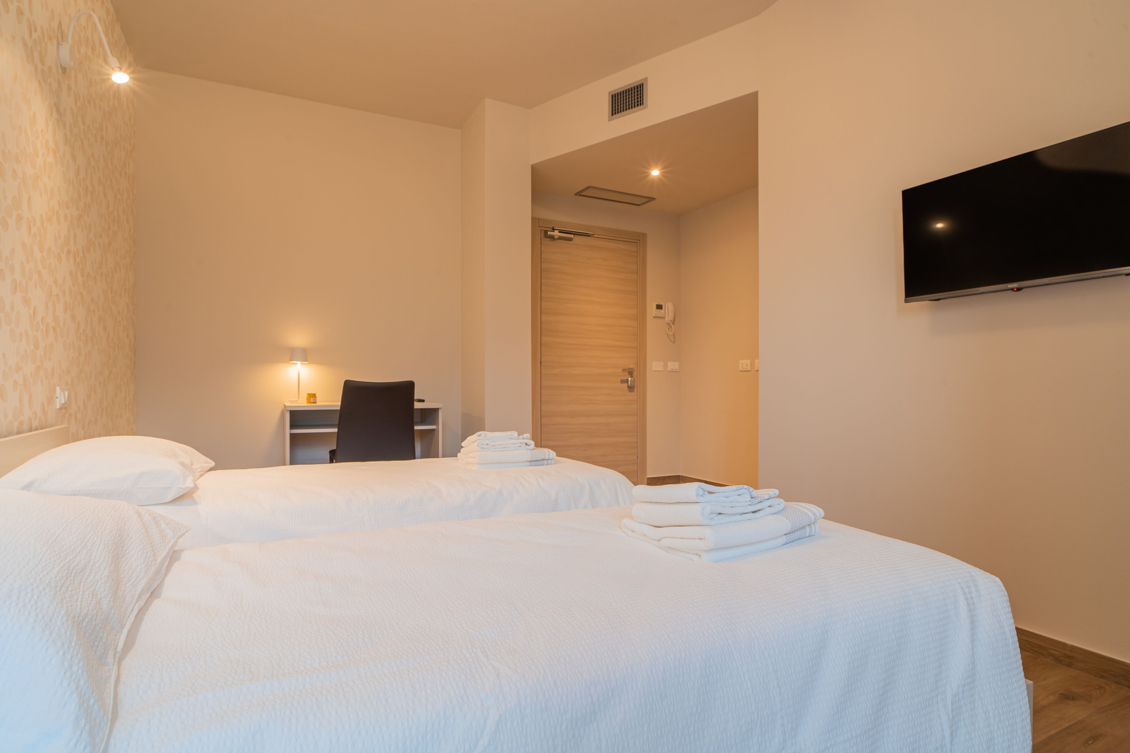 A hotel room with two beds, a TV mounted on the wall, and a desk with a chair.