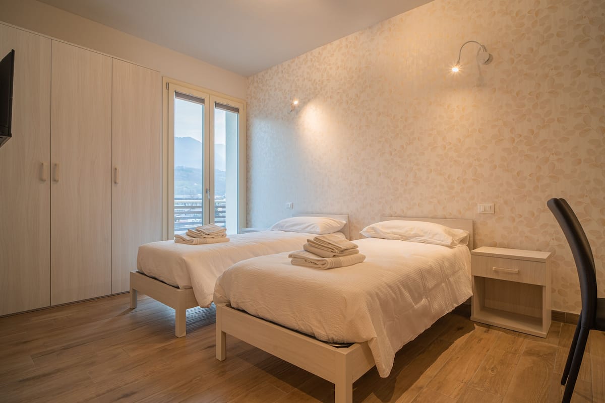 A bedroom with two beds, a wardrobe, a nightstand, and a chair.