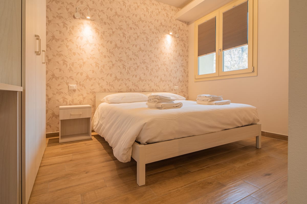 A bedroom with a bed, bedside table, and a window with blinds.