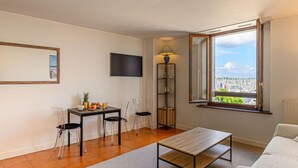 A modern living room with a wooden coffee table, a sofa, and a dining area with chairs and a small table. A TV is mounted on the wall, and there's a window with a view of a marina. - Le Quai by Interhome (La Trinité Sur Mer)