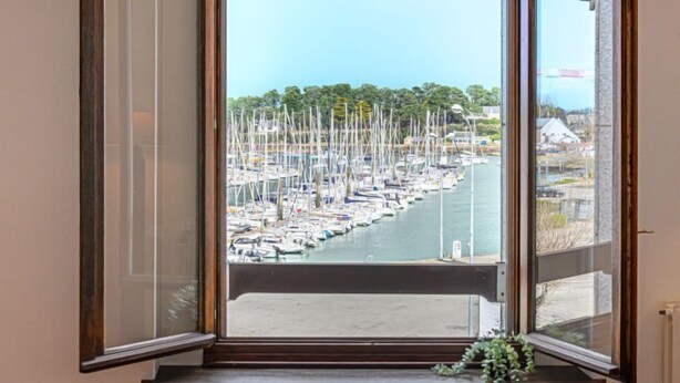 A bay with numerous boats docked, a clear sky, and a view of a town in the distance. - Le Quai by Interhome (La Trinité Sur Mer)