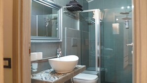 A modern bathroom with a glass-enclosed shower, a white sink, and a mirror above the sink. - Sa Domu de Jana - Studio apartment with garden and panoramic view of Poetto (Quartu Sant'Elena)