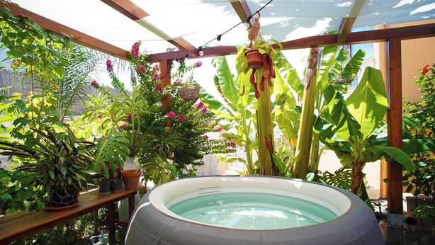 A hot tub surrounded by lush tropical plants and a wooden pergola structure. - Sa Domu de Jana - Studio apartment with garden and panoramic view of Poetto (Quartu Sant'Elena)