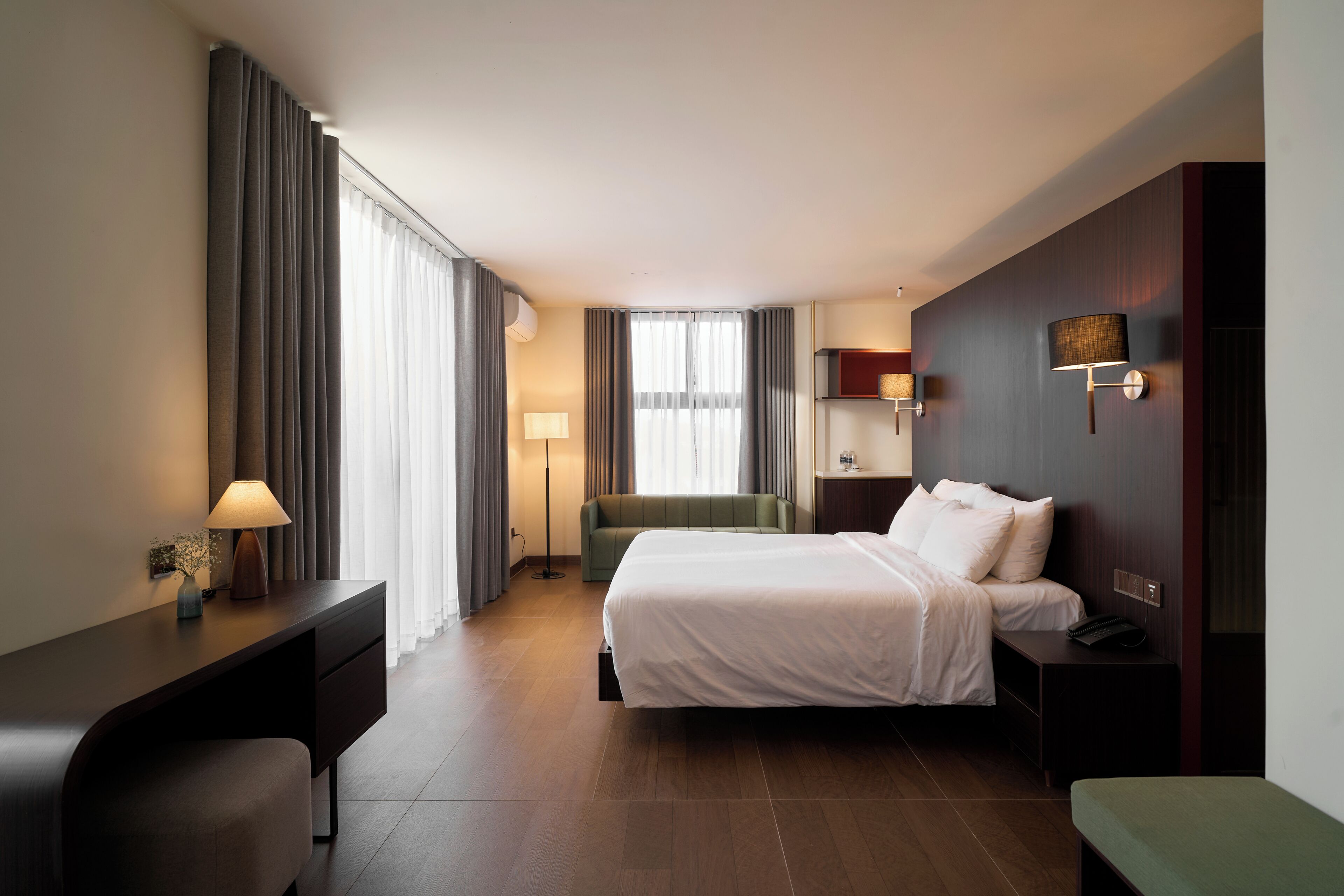 Una habitación de hotel con cama, mesita de noche, lámpara y un banco verde.