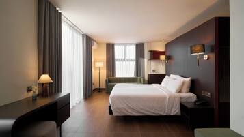 Una habitación de hotel con cama, mesita de noche, lámpara y un banco verde.