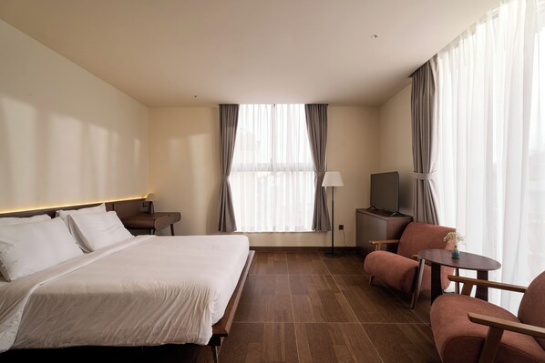 Habitación de hotel con cama, escritorio, silla, televisor y ventana con cortinas.