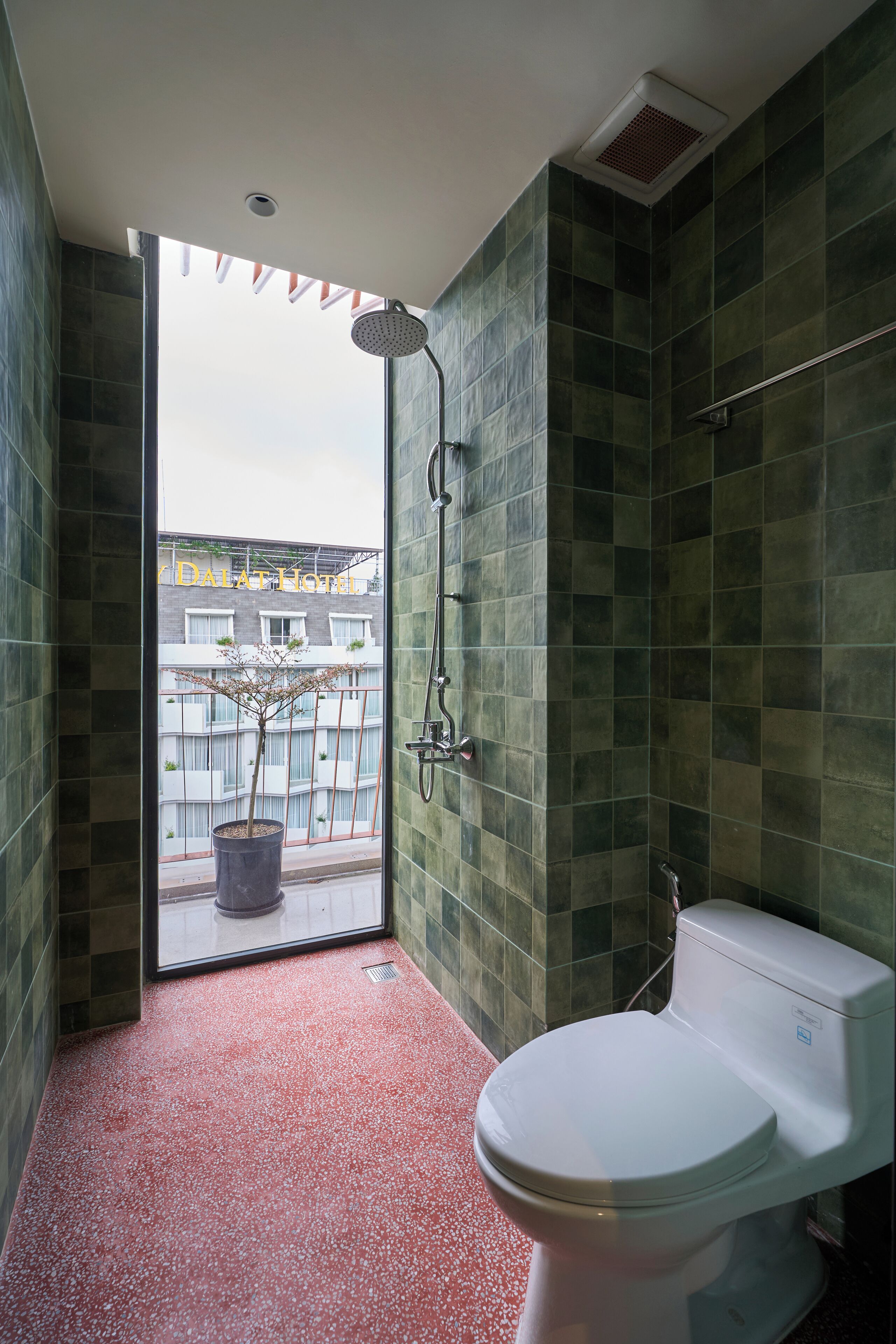 Une salle de bain avec des toilettes blanches, une douche et une vue sur un bâtiment à l’extérieur.