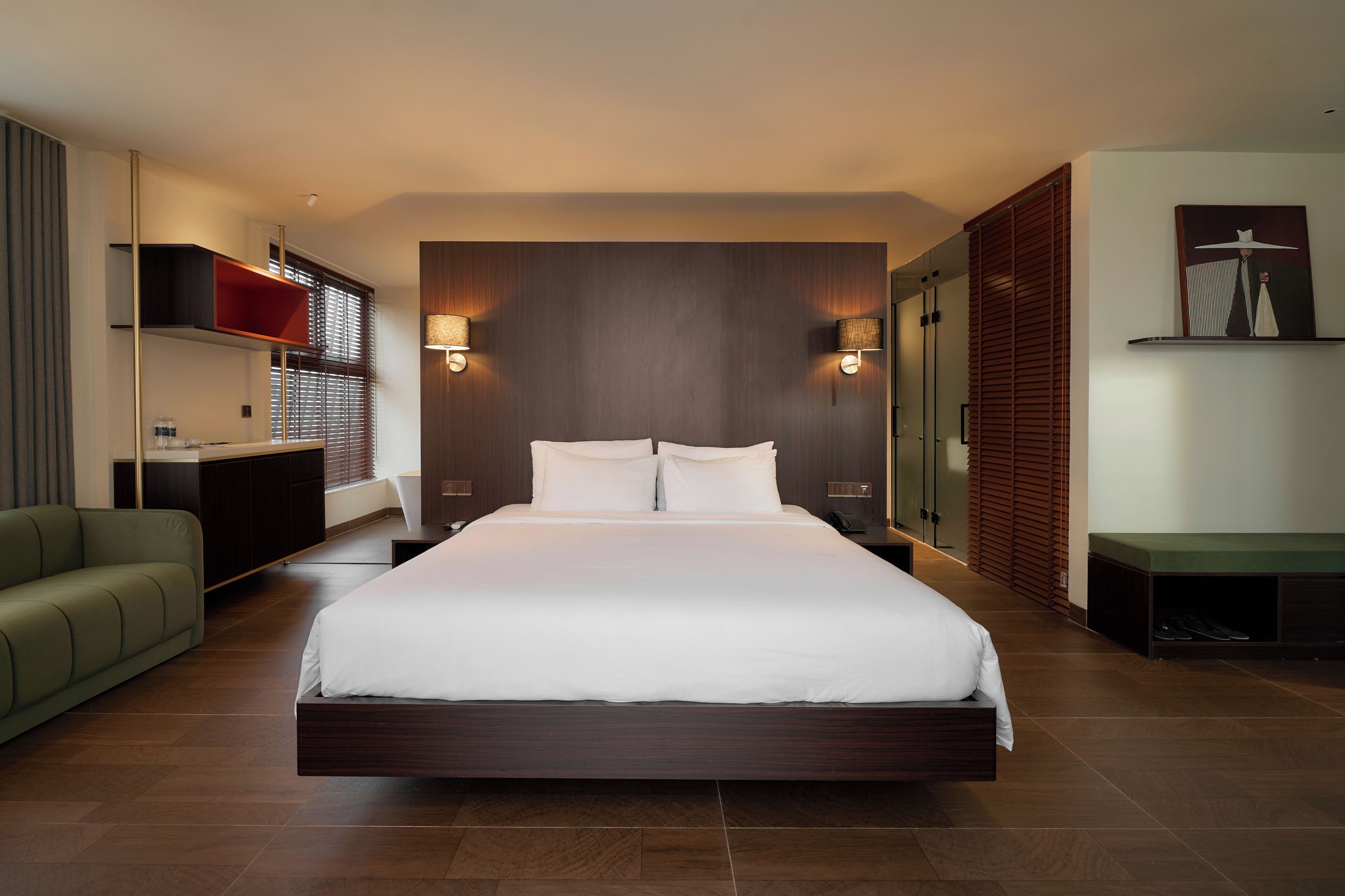 A modern hotel room with a large bed, bedside lamps, a desk, and a green sofa.
