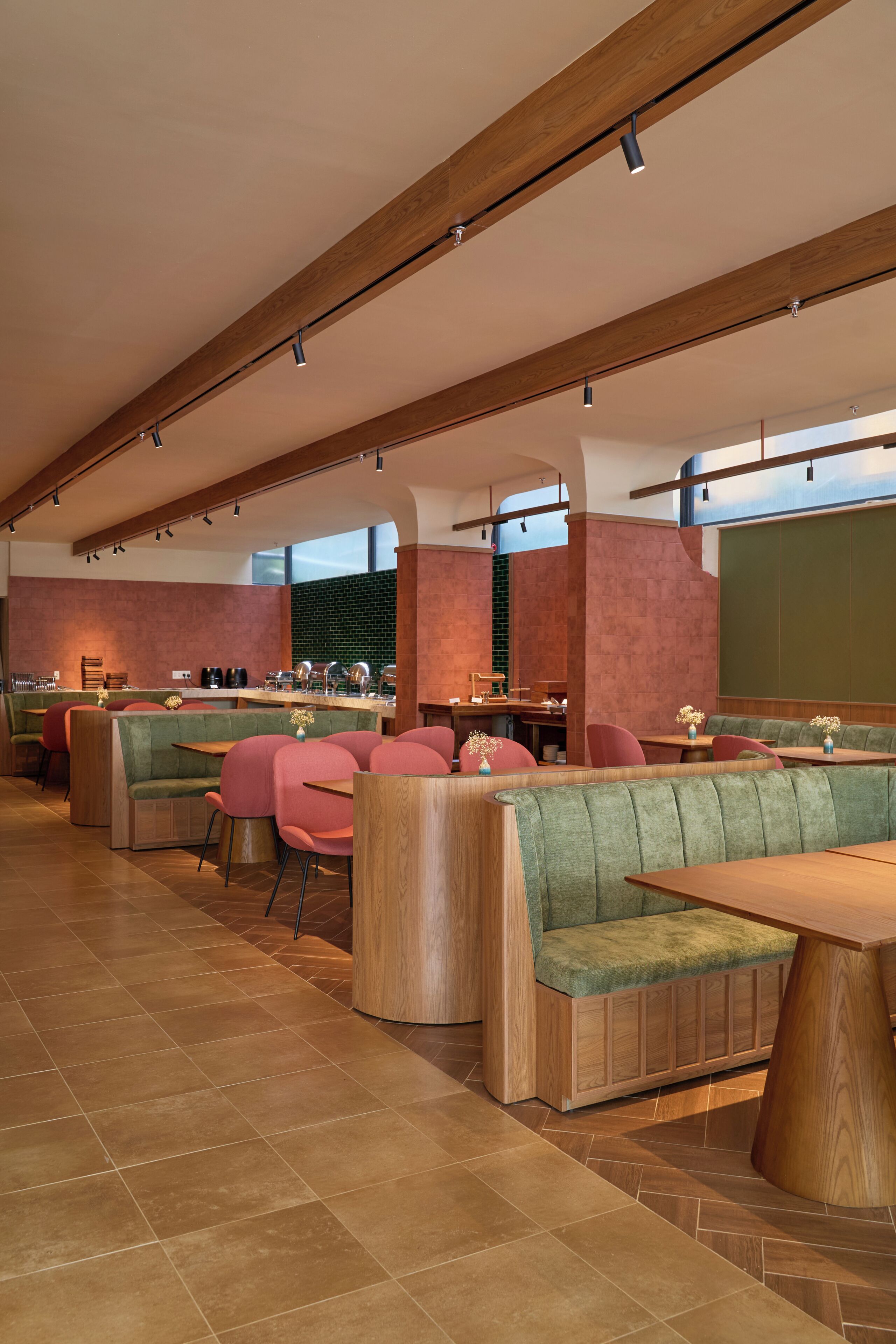 A modern restaurant interior with wooden beams, green cushioned seating, and a bar area.