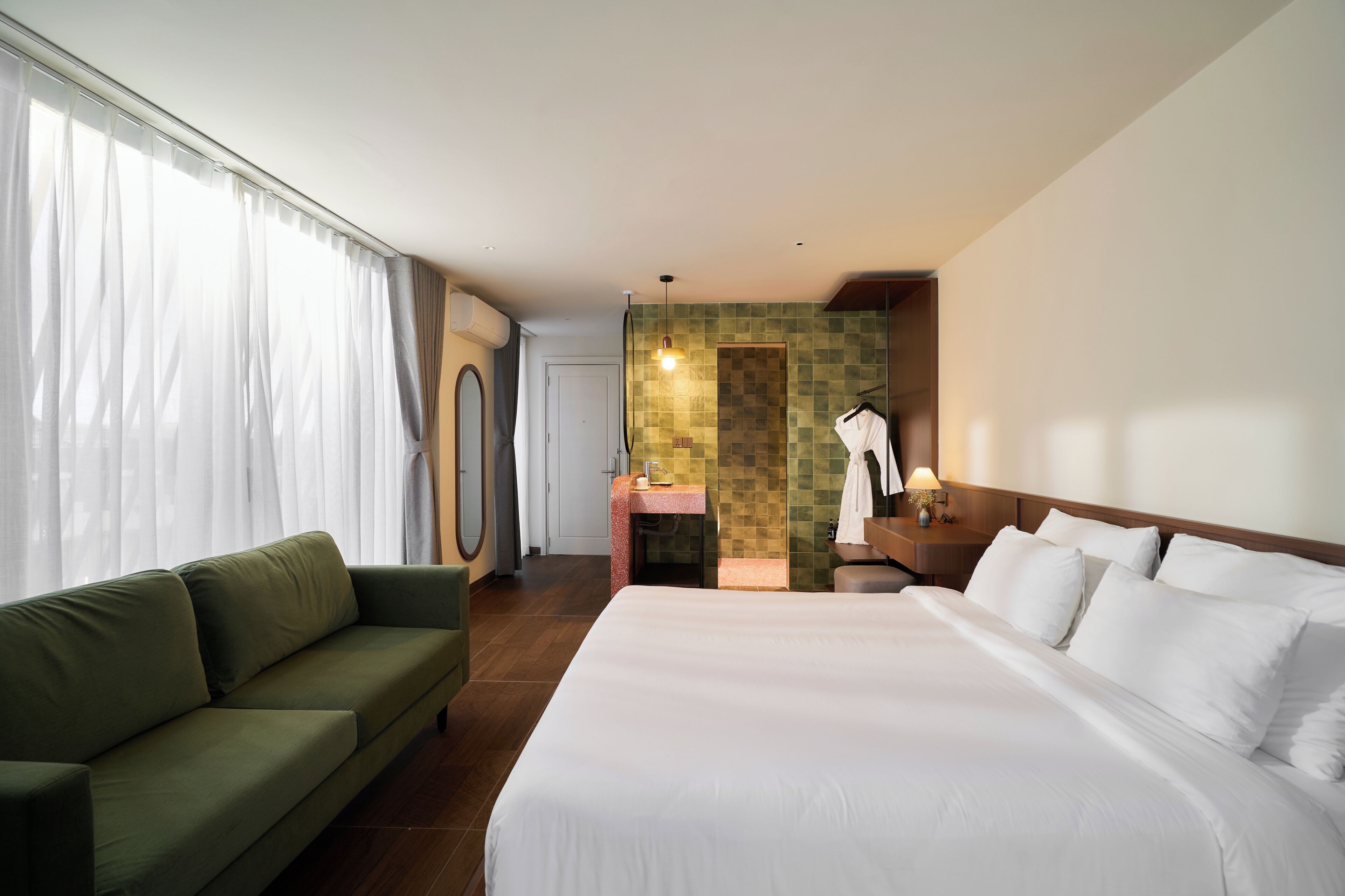 A hotel room with a bed, a sofa, a bathroom with a shower, and a view of the outdoors.