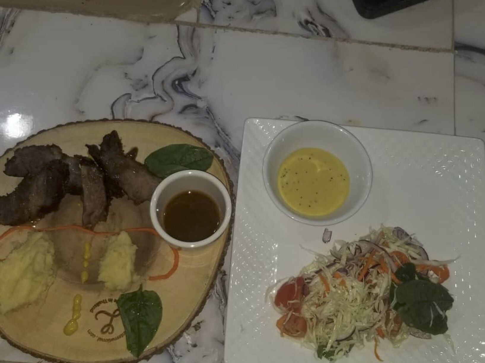 A plate with sliced meat, a bowl of sauce, and a salad with shredded vegetables and greens.