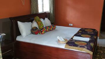 A hotel room with a wooden bed, a window with curtains, an air conditioning unit, and a wall-mounted mirror.