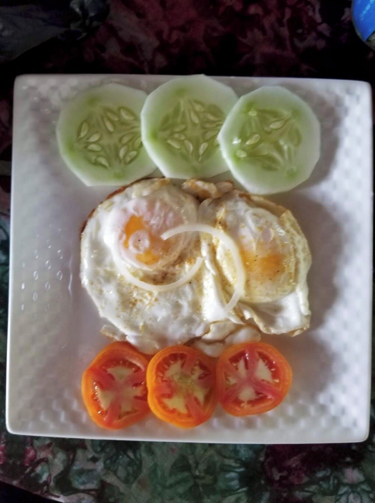 Um prato com ovo frito, fatias de pepino e fatias de tomate.