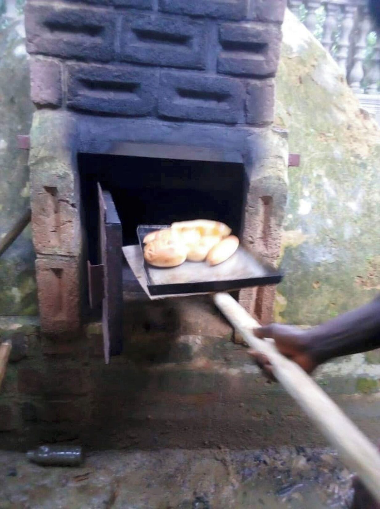 A stone-built outdoor oven with bread being placed inside.