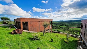 Un bâtiment moderne en briques, agrémenté d’une extension en verre, entouré de champs verdoyants et sous un ciel dégagé.