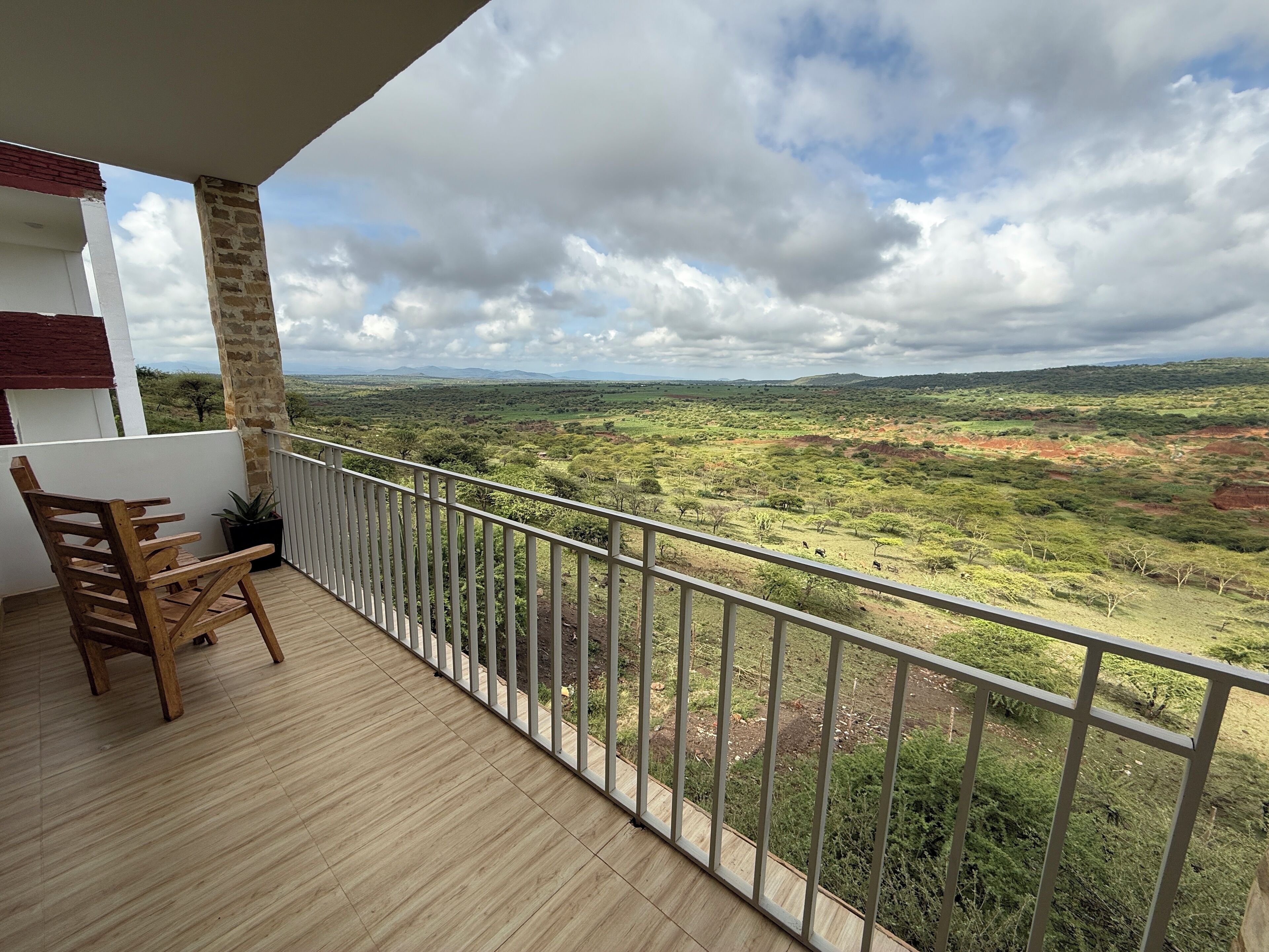 A balcony with a wooden floor, a chair, and a view of a savanna landscape.
