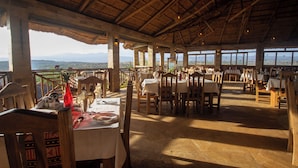 Un restaurant en plein air avec des tables et des chaises en bois, de grandes fenêtres offrant une vue sur les montagnes.