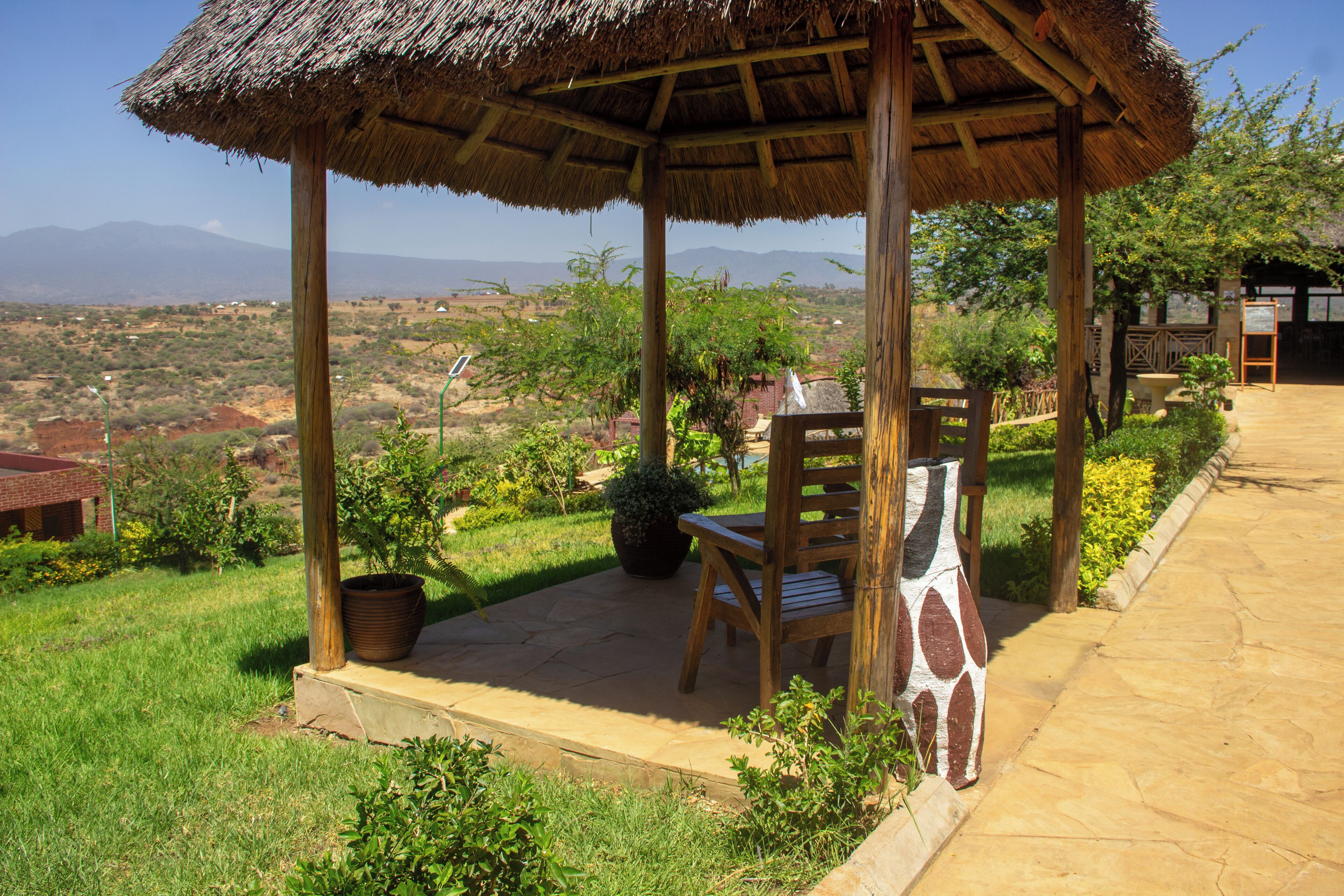 A wooden gazebo with a thatched roof, a wooden chair, and a potted plant.
