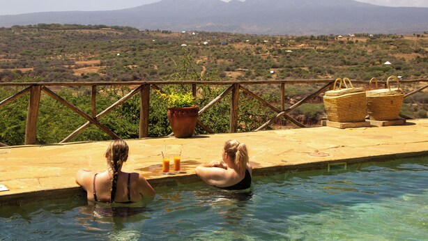 Une piscine avec vue sur les montagnes, une terrasse en bois et deux paniers en osier.