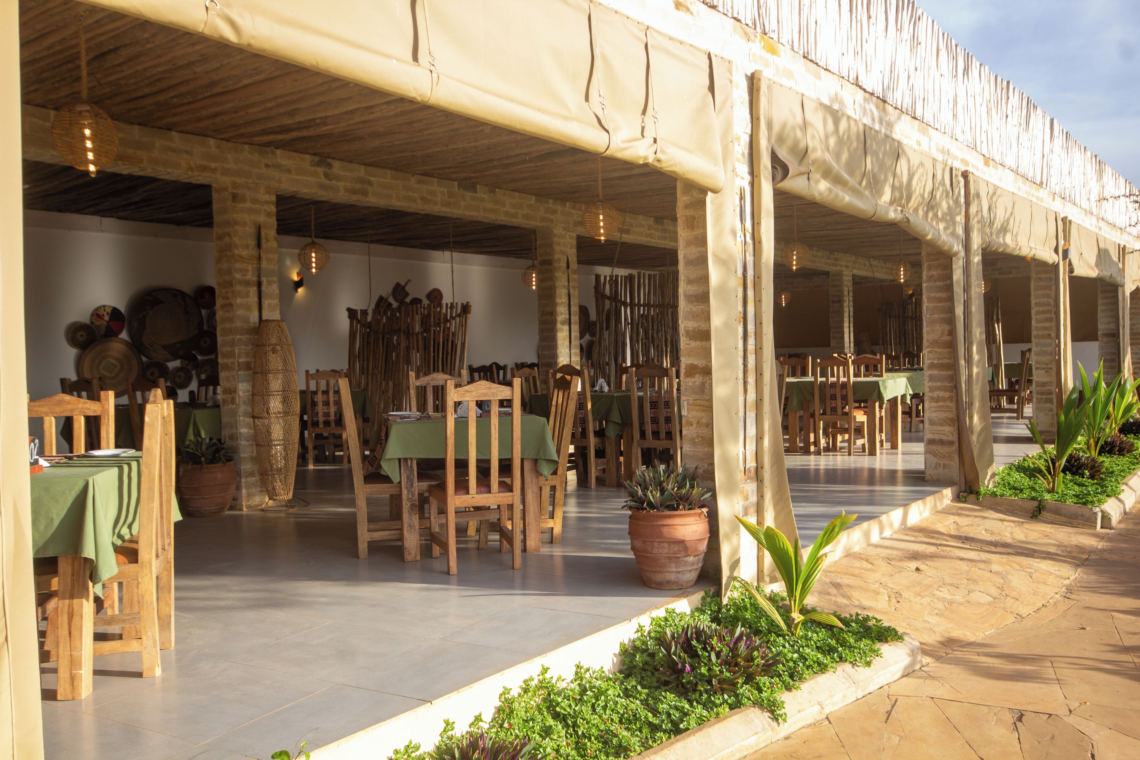 An outdoor dining area with wooden tables and chairs, potted plants, and a covered seating area.
