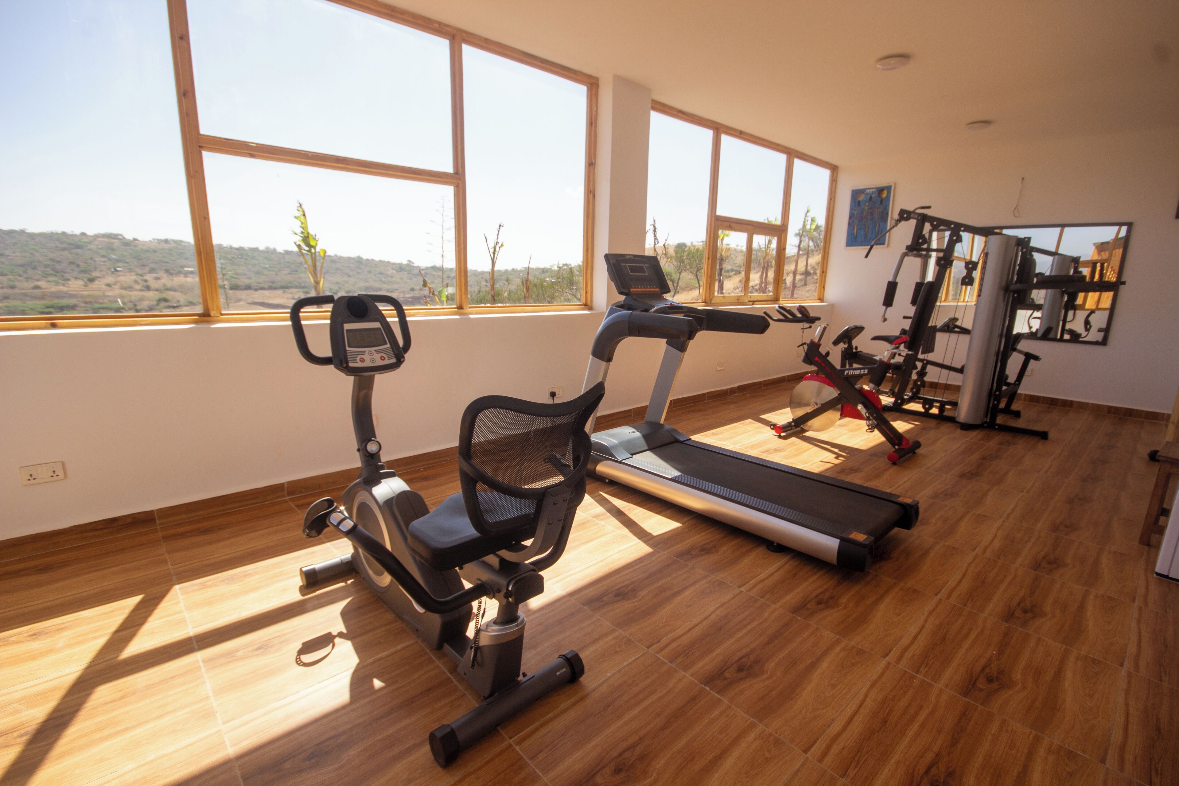 Een sportschool met trainingsapparatuur, grote ramen en uitzicht op het omliggende landschap.