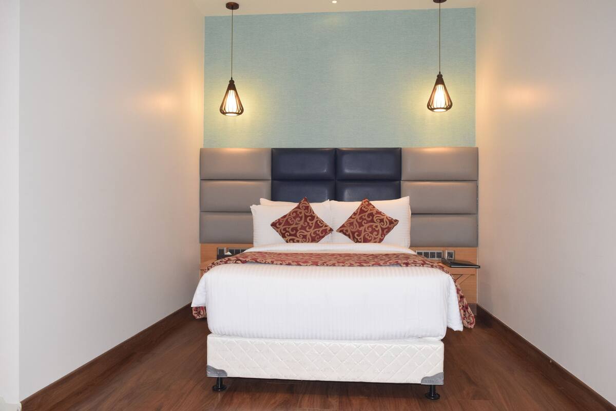 Une chambre d’hôtel moderne avec un grand lit, deux lampes suspendues, une tête de lit dotée d’une étagère intégrée et un plancher en bois.