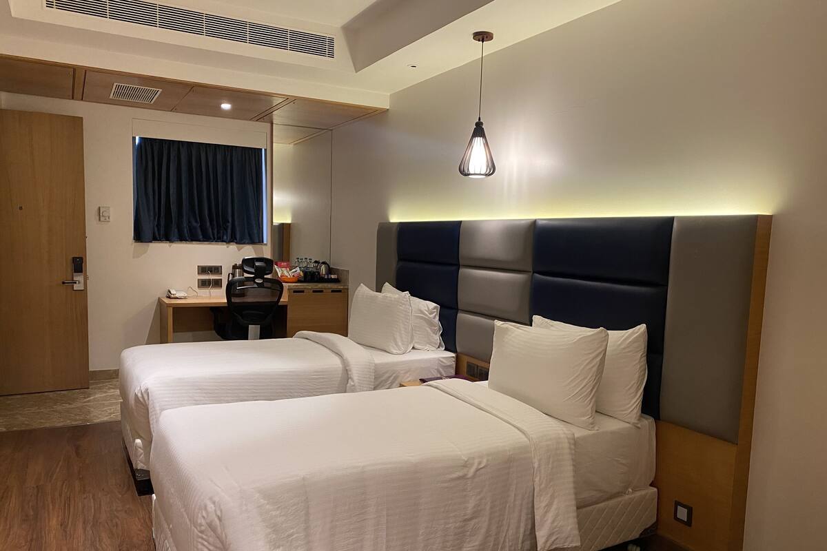 Une chambre d’hôtel avec deux lits, un bureau, une chaise et un miroir.