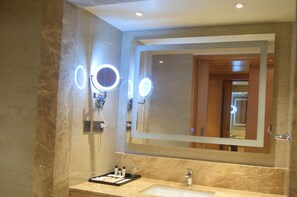 Een badkamer met een grote spiegel, twee ronde lampen, een wastafel en een opbergmeubel met toiletartikelen.