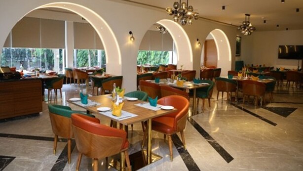Une salle à manger spacieuse, dotée de plusieurs tables et chaises, de grandes fenêtres et d’un lustre.