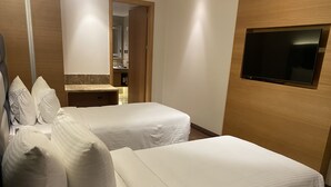 Une chambre d’hôtel avec deux lits, un téléviseur fixé au mur et une salle de bain visible à travers une porte ouverte.