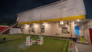 A building with a flat roof, a yellow and white facade, and a covered outdoor seating area with chairs and a small fire. - Hotel Chotiwala – 10 Mins from Kashi Vishwanath Temple (Varanasi)
