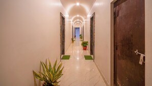 A hallway with a marble floor, green mats, potted plants, and a dark door on the right. - Hotel Chotiwala – 10 Mins from Kashi Vishwanath Temple (Varanasi)