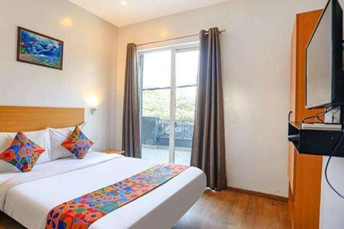 A hotel room with a bed, a television, and a window with curtains.