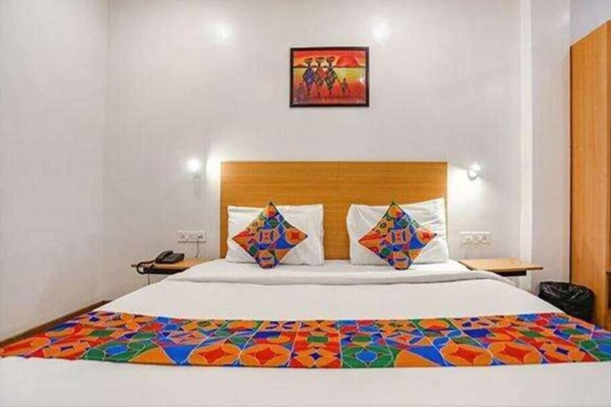 A hotel room with a bed, a wooden headboard, a colorful bedspread, a wall-mounted painting, and a wooden wardrobe.