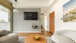 Un saló modern amb una taula de centre rodona de fusta, dos sofàs beix i un televisor fixat a la paret, juntament amb una porta de fusta.