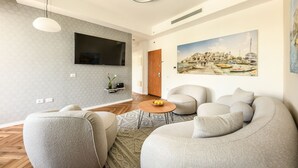 Un saló modern amb televisió plana, seients confortables i un quadre gran d'una població costanera.