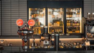 Una zona de bar con mostrador, una máquina de café y una exhibición de botellas al fondo.
