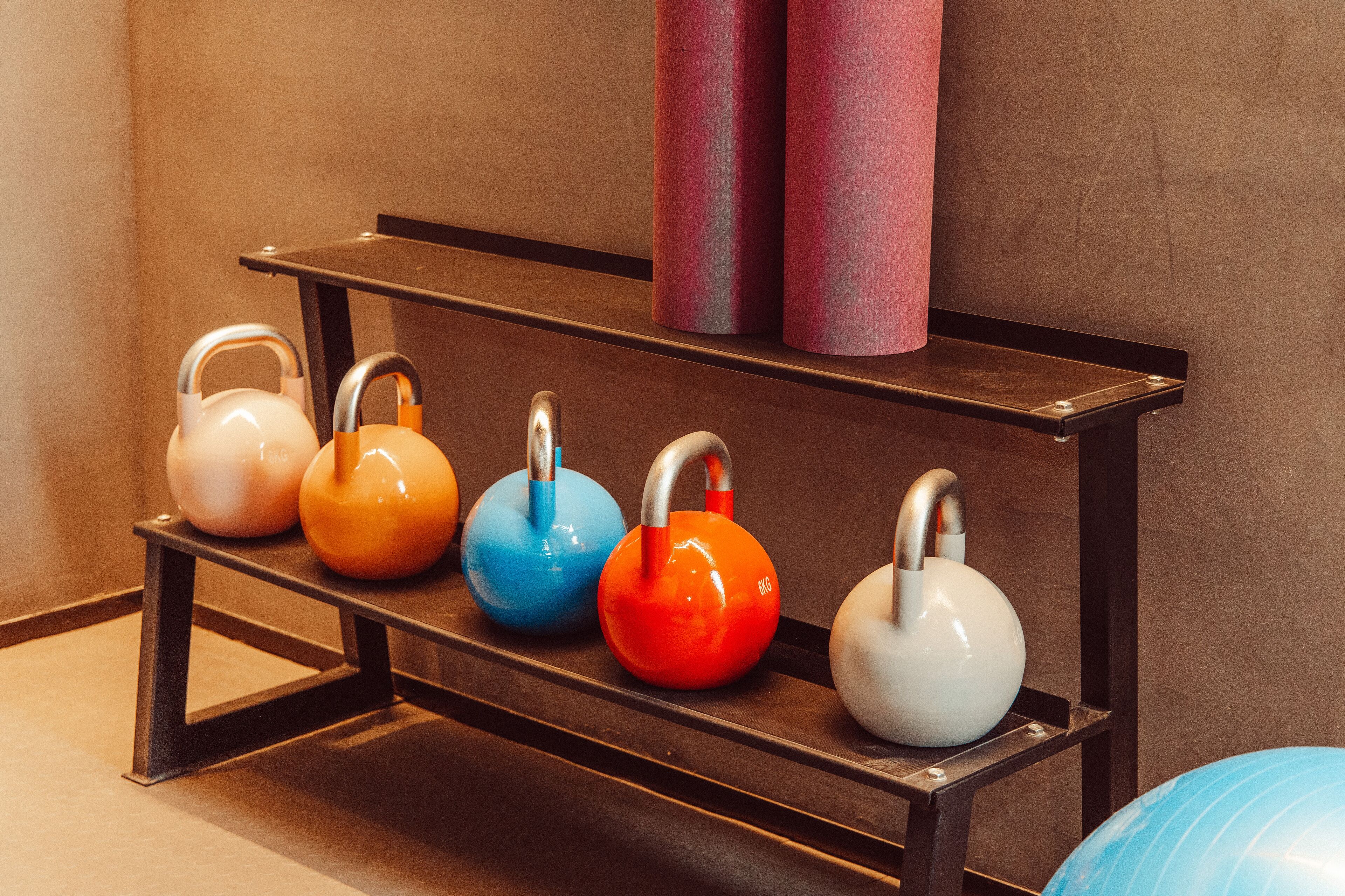 A row of kettlebells on a metal rack against a wall.