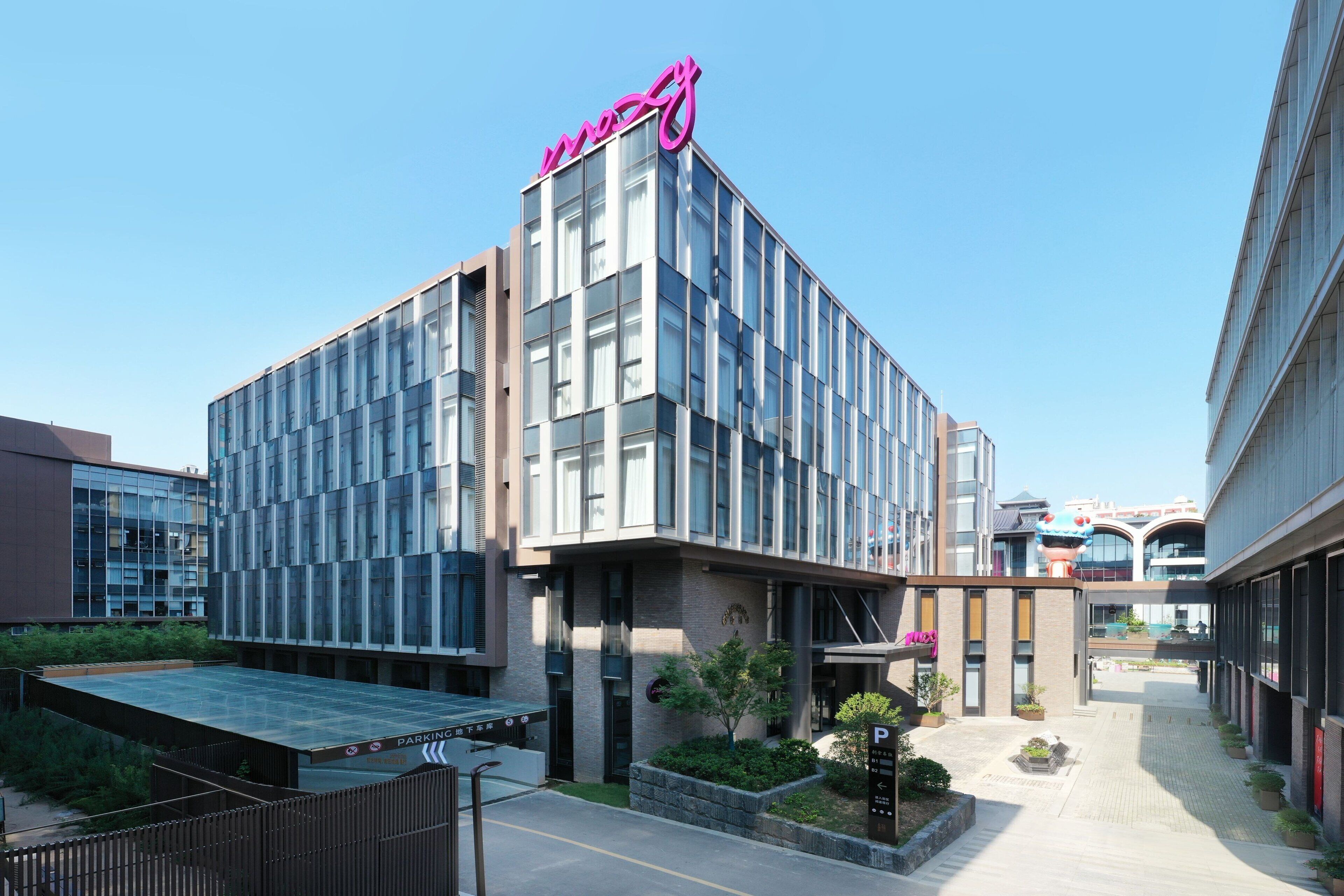 Un edificio moderno con un llamativo logotipo rosa, un área exterior cubierta y un letrero de estacionamiento.