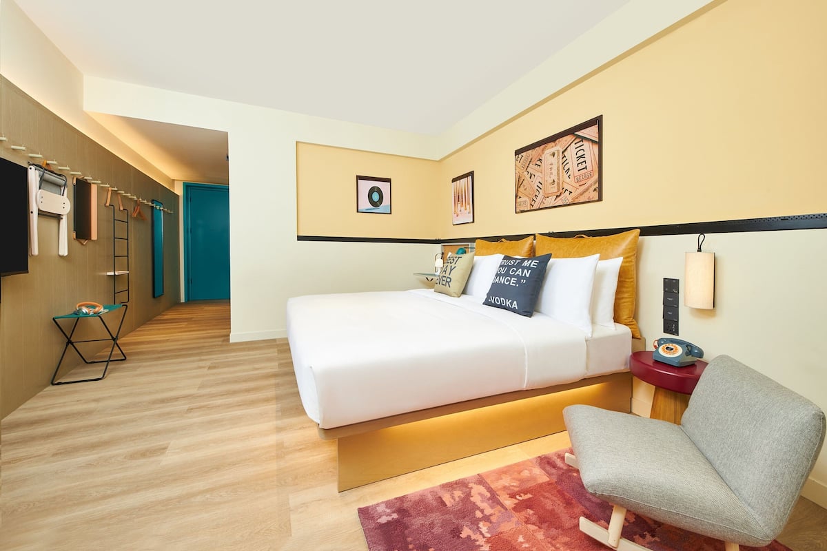 A hotel room with a bed, a chair, a desk, and a wall-mounted telephone.