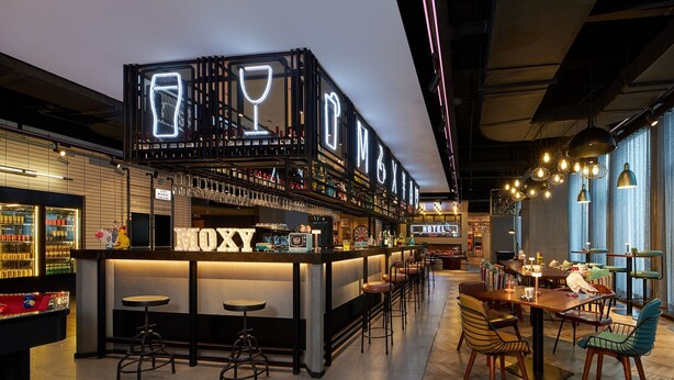 A bar area with a neon sign, stools, and a dining area with chairs and tables. - Moxy Xi'an Downtown (Xi'an)
