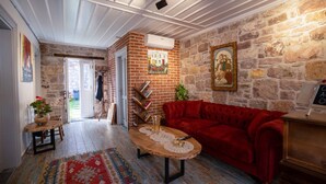 A cozy living room with a red sofa, a wooden coffee table, and a stone wall. - Cunda Alesta Otel (Ayvalik)