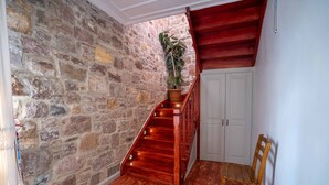 A wooden staircase with a stone wall backdrop, a potted plant, and a wooden chair. - Cunda Alesta Otel (Ayvalik)