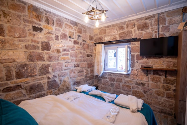 Habitación con paredes de piedra, una cama, un televisor de pantalla plana y un ventanal con cortinas.