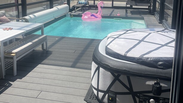 Un espace piscine extérieur abrité, doté de chaises longues, d’un jacuzzi et d’un flotteur en forme de flamant rose.