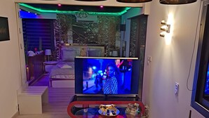 Un salon moderne doté d’un grand téléviseur à écran plat, d’un coin repas avec une table en verre et d’un éclairage d’ambiance.