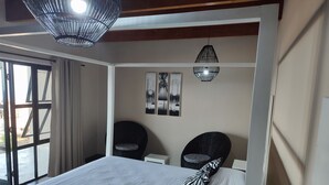 Une chambre à coucher avec un lit, deux chaises, un luminaire au plafond et des œuvres d’art accrochées au mur.