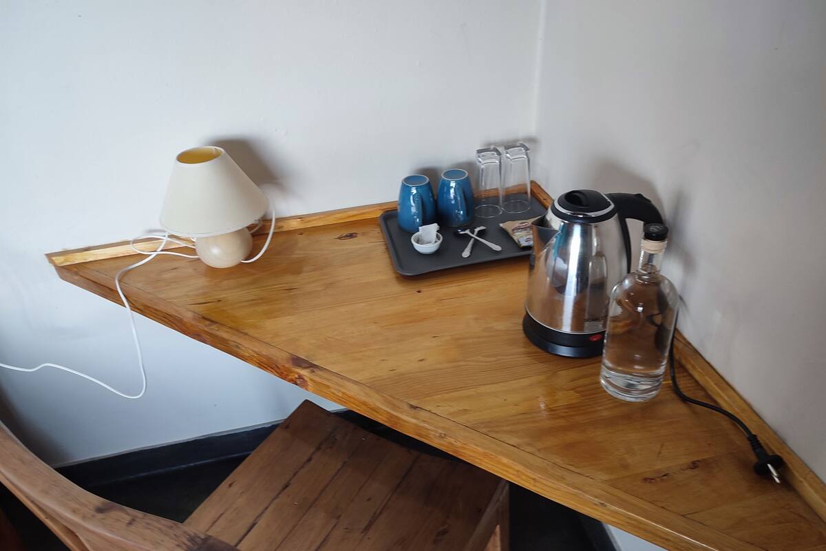 A wooden table with a lamp, a kettle, and a bottle.
